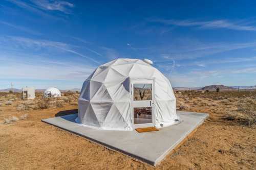 A white geodesic dome on a concrete pad in a desert landscape under a clear blue sky.