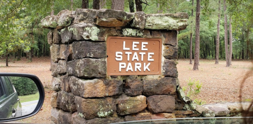 Stone entrance sign for Lee State Park, surrounded by trees and a gravel area.