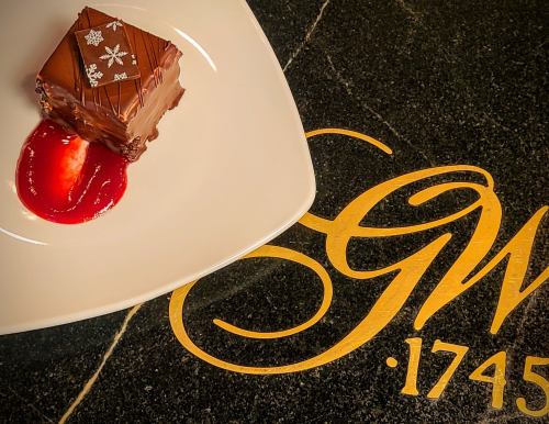 A chocolate dessert with snowflake decorations on a plate, accompanied by a red fruit sauce, on a dark surface.