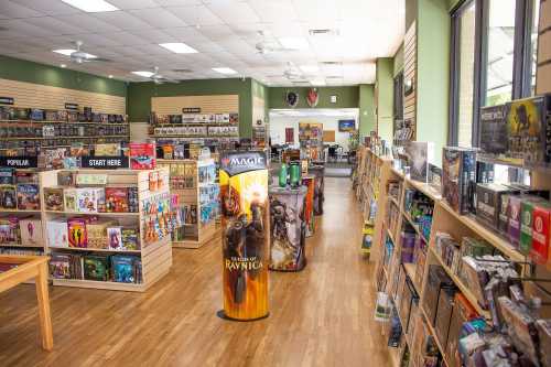 A spacious game store filled with shelves of board games and card games, featuring a Magic: The Gathering display.