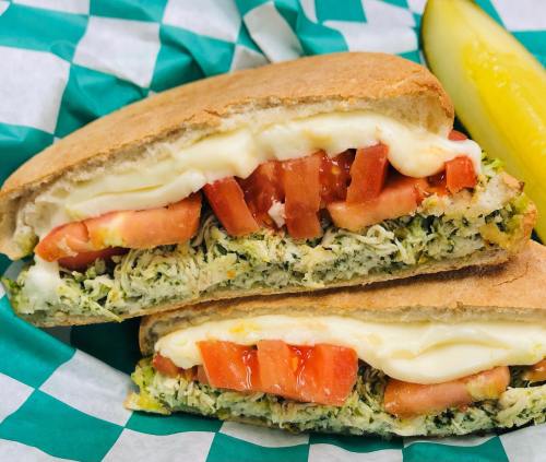 A sandwich with shredded chicken, tomatoes, and mayonnaise, served with a pickle on a checkered green and white plate.