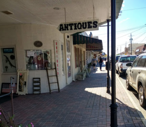 A street view of an antique shop with a sign, brick pavement, and people walking by.