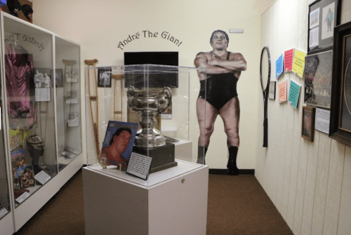 A museum display featuring a trophy, photos, and a life-size cutout of André the Giant.