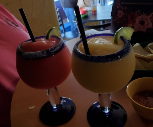 Two colorful frozen cocktails in large glasses, one red and one yellow, garnished with lime slices and served with straws.