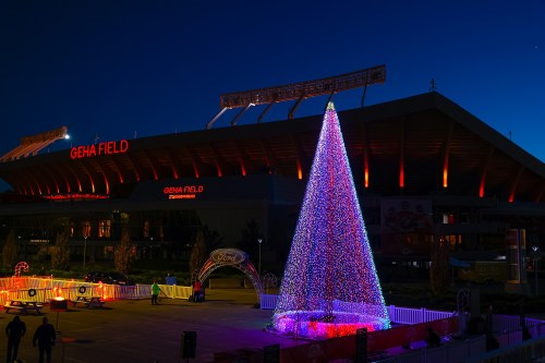 A brightly lit Christmas tree in front of Geha Field, illuminated against a twilight sky.
