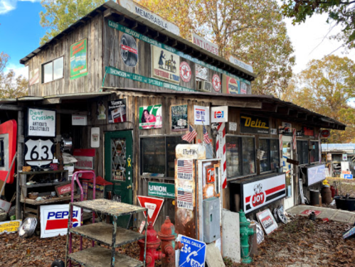 A rustic antique shop adorned with vintage signs and memorabilia, surrounded by autumn foliage.