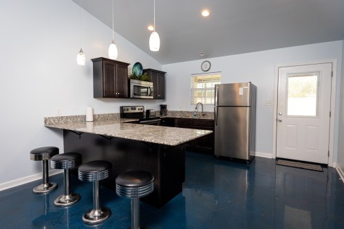 Modern kitchen with granite countertops, stainless steel appliances, and bar stools at the island. Bright blue floor.