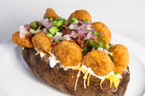 A loaded baked potato topped with shrimp, green onions, and diced vegetables on a white plate.