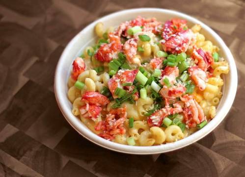 A bowl of macaroni pasta topped with lobster meat and chopped green onions.