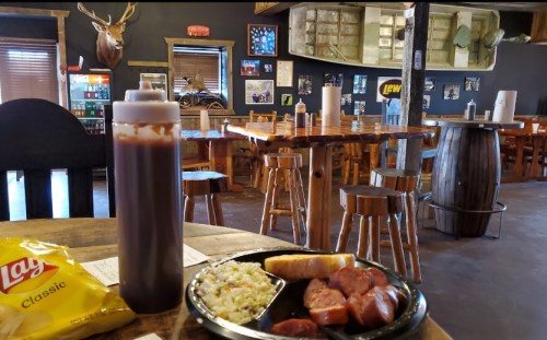 A plate of food with sausage, coleslaw, and bread sits on a table in a rustic restaurant with wooden decor.