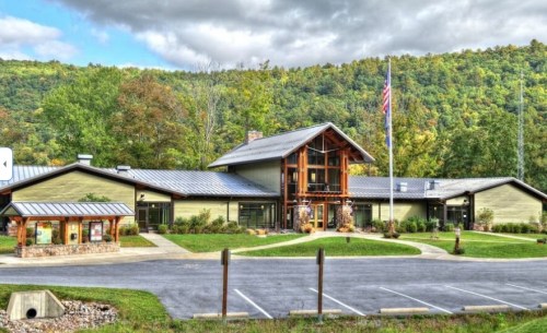 A modern building surrounded by trees, featuring large windows and a flagpole, set against a hilly landscape.