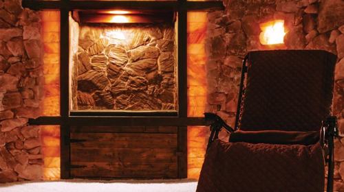 Cozy room with stone walls, warm lighting, and a comfortable chair near a decorative stone feature.