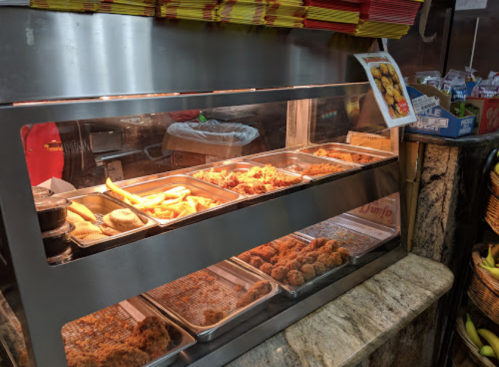 A display case filled with various fried foods, including chicken and plantains, in a casual dining setting.