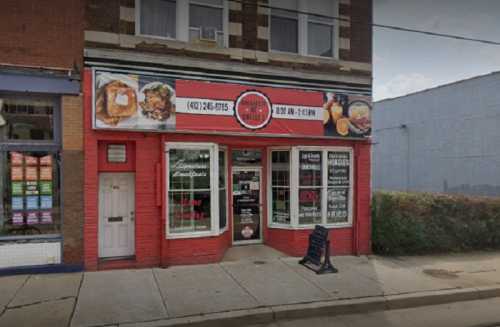 A storefront with a red facade, featuring a sign for a restaurant, displaying hours and menu items.