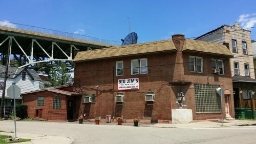 A brick building with a sign reading "Big Jim's," located at a street corner under a bridge, with potted plants outside.