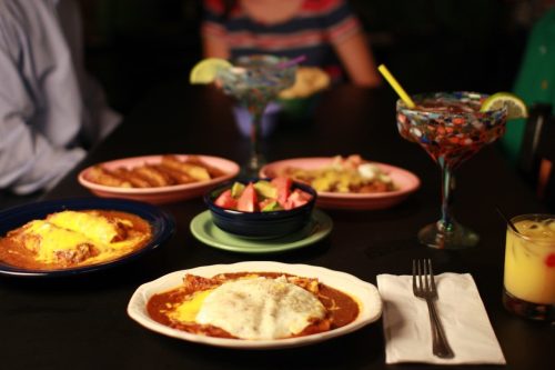 A table set with colorful plates of Mexican food, drinks, and a variety of dishes, creating a vibrant dining scene.