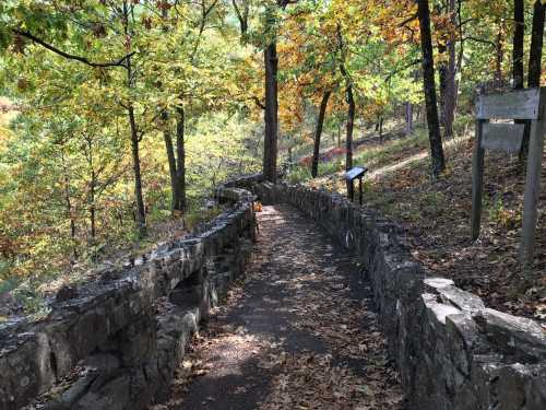 A winding stone path through a colorful forest with autumn leaves and informational signs along the way.