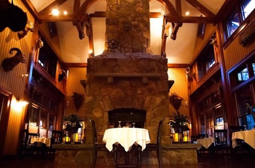 Cozy restaurant interior featuring a large stone fireplace, wooden beams, and elegantly set tables.