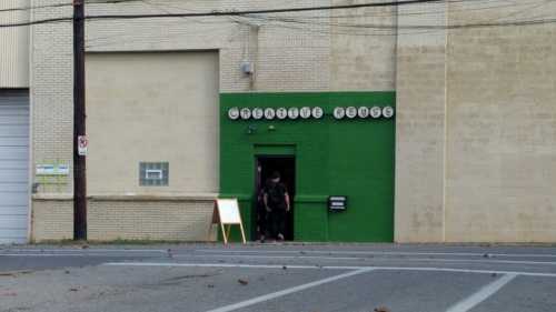 A green door with a sign reading "Creative House" in a brick building, with two people entering.