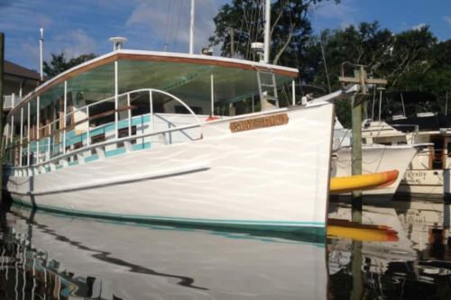 A white boat with turquoise accents docked in calm water, reflecting the surrounding trees and other boats.