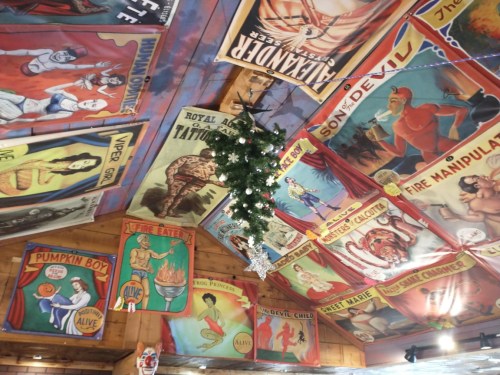 Colorful vintage posters adorn a wooden ceiling, with a small Christmas tree hanging in the center.