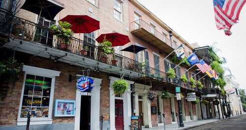 Historic brick buildings with balconies, colorful umbrellas, and flags in a vibrant street scene.