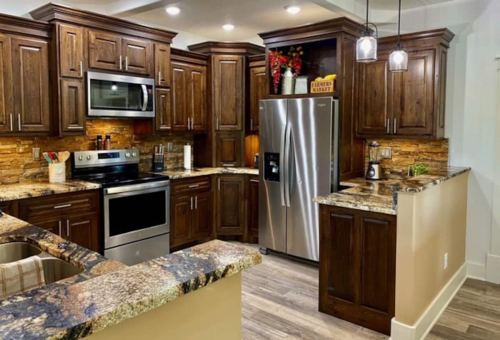 Modern kitchen with dark wood cabinets, stainless steel appliances, and granite countertops, featuring warm lighting.