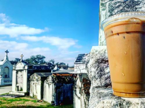 Iced coffee sits on a stone ledge in a cemetery, with tombstones and a blue sky in the background.
