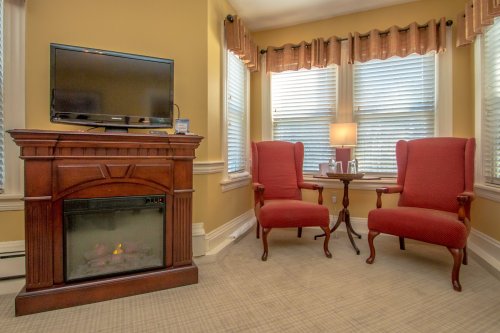Cozy corner with two red chairs, a small table, a TV, and a faux fireplace in a well-lit room with yellow walls.
