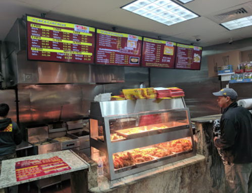 A fast food counter with a menu board, displaying food options and prices, and a customer waiting in front.