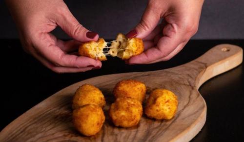 Hands pulling apart a cheesy, golden-brown snack on a wooden serving board.