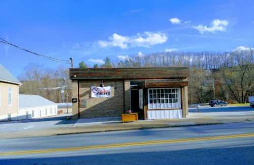 A small brick building with a sign reading "Grill" and a large window, set against a blue sky and trees in the background.