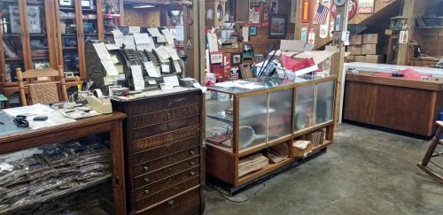 A cozy antique shop interior featuring wooden furniture, display cases, and various items for sale.