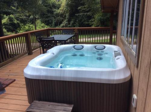 A hot tub on a wooden deck, surrounded by trees and a table with chairs in the background.