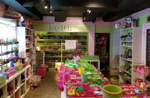 Colorful candy store interior with shelves of soda bottles and a variety of candies displayed on tables.