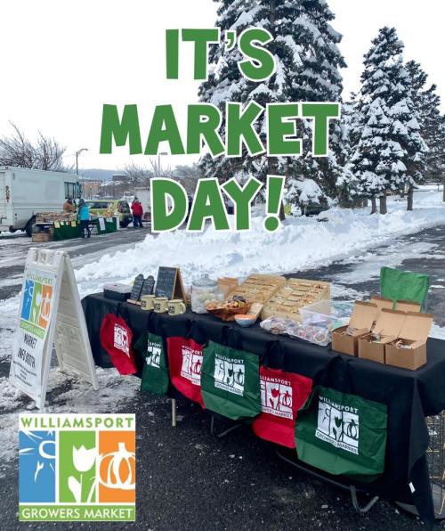 A snowy market scene with a table displaying goods, featuring a sign that reads "It's Market Day!" and the Williamsport logo.