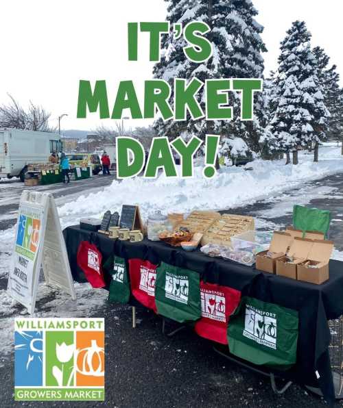 A snowy market scene with a table displaying goods, featuring a sign that reads "It's Market Day!" and the Williamsport logo.