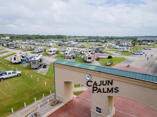 Aerial view of Cajun Palms RV resort, featuring numerous RVs parked on green lawns under a cloudy sky.