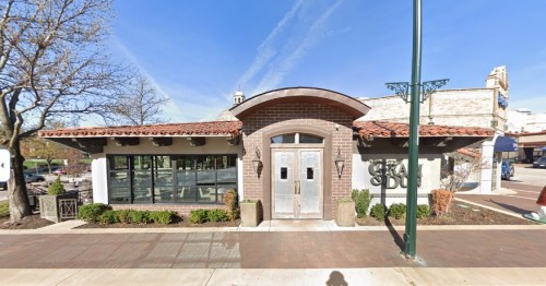 A modern restaurant with a curved roof, large windows, and a brick facade, set in a sunny urban environment.