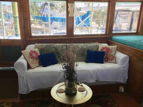 Cozy boat interior featuring a white sofa with decorative pillows and a small table with a vase, overlooking the marina.