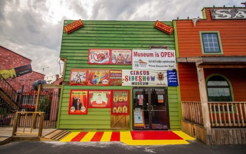 Colorful exterior of a circus sideshow museum with various signs, an open banner, and a playful entrance.