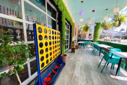 A vibrant café with green decor, featuring a large Connect Four game and tables set for dining.