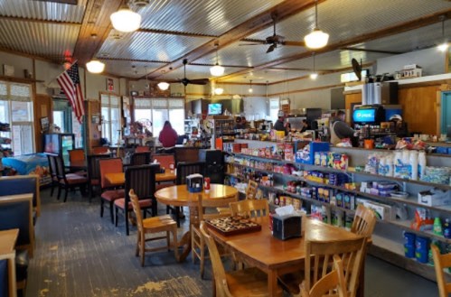 A cozy diner interior with tables, chairs, and shelves stocked with snacks, featuring a vintage decor and an American flag.