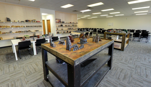 A spacious room with tables displaying miniature models and shelves filled with various items, surrounded by empty chairs.