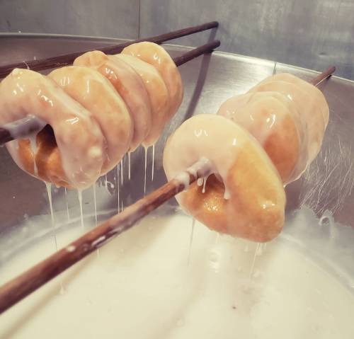 Doughnuts on wooden skewers dripping with glaze, resting in a large bowl.