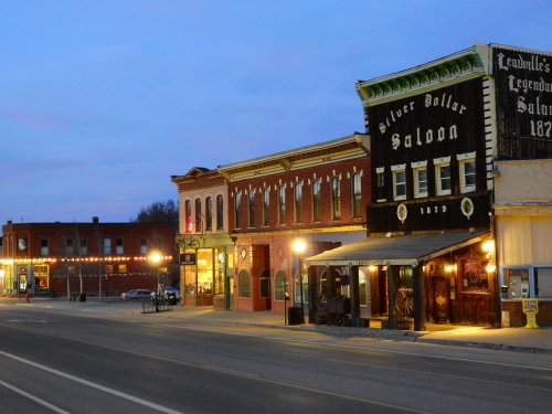 Historic buildings line a quiet street at dusk, featuring the Silver Dollar Saloon and warm streetlights.