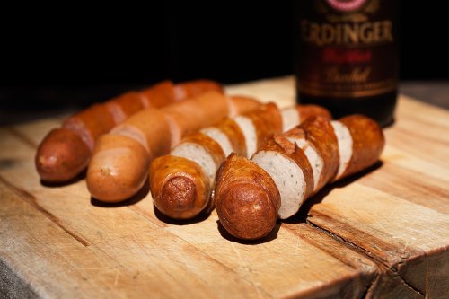 A wooden board with various types of sausages and a bottle of Erdinger beer in the background.