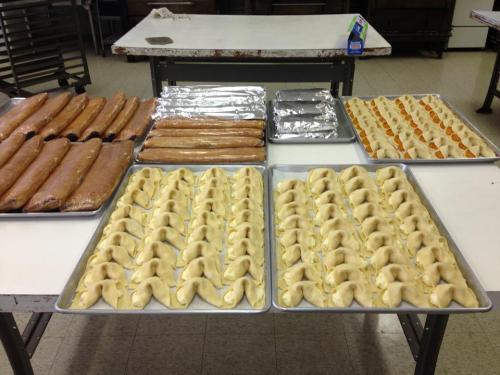 Trays of freshly prepared dough and pastries arranged on a table in a kitchen setting.