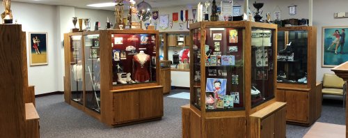 A room with display cases showcasing trophies, memorabilia, and vintage clothing, with walls adorned with framed photos.