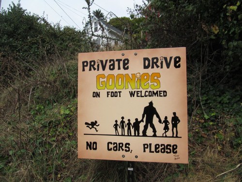Sign reading "Private Drive: Goonies on foot welcomed, no cars please," with playful illustrations of characters.